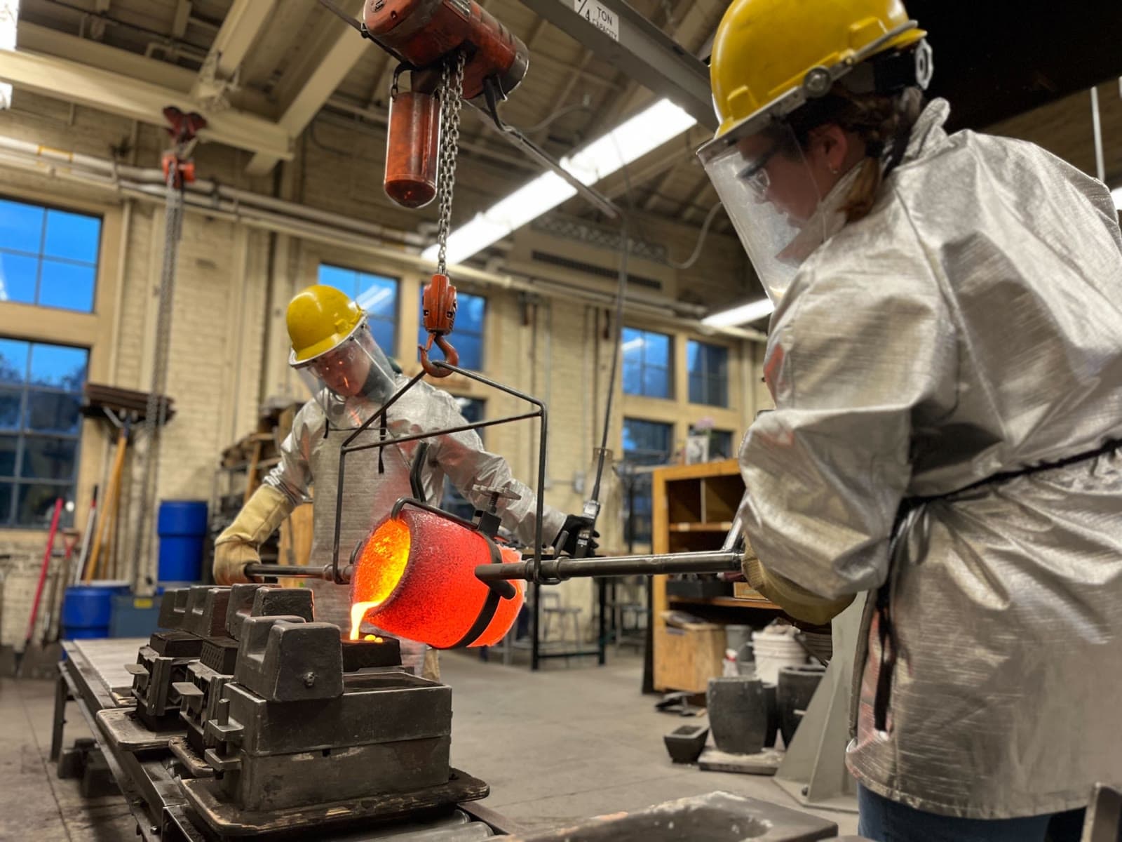 Students pouring molten metal in a fabrication workshop
